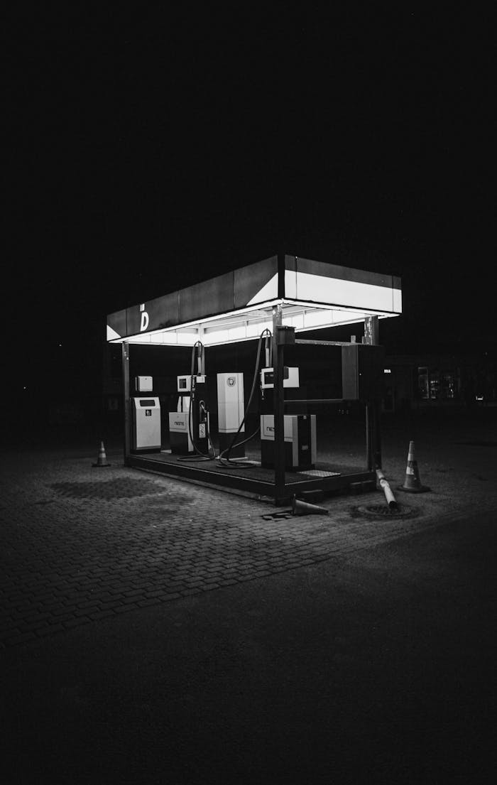 A solitary, illuminated gas station captured in moody black and white at night.